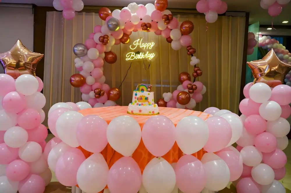 A birthday party with a balloon arch, a neon “Happy Birthday” sign and a cake