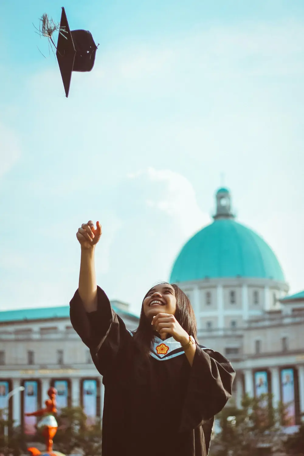 A graduate throwing her cap in front of a domed building